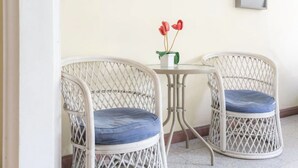 Dos sillas de mimbre con cojines azules y una pequeña mesa con un jarrón de flores rojas.