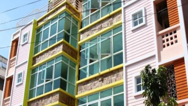 Un edificio de varios pisos con una fachada distintiva amarilla y verde, ventanas amplias y un balcón visible en los pisos superiores.