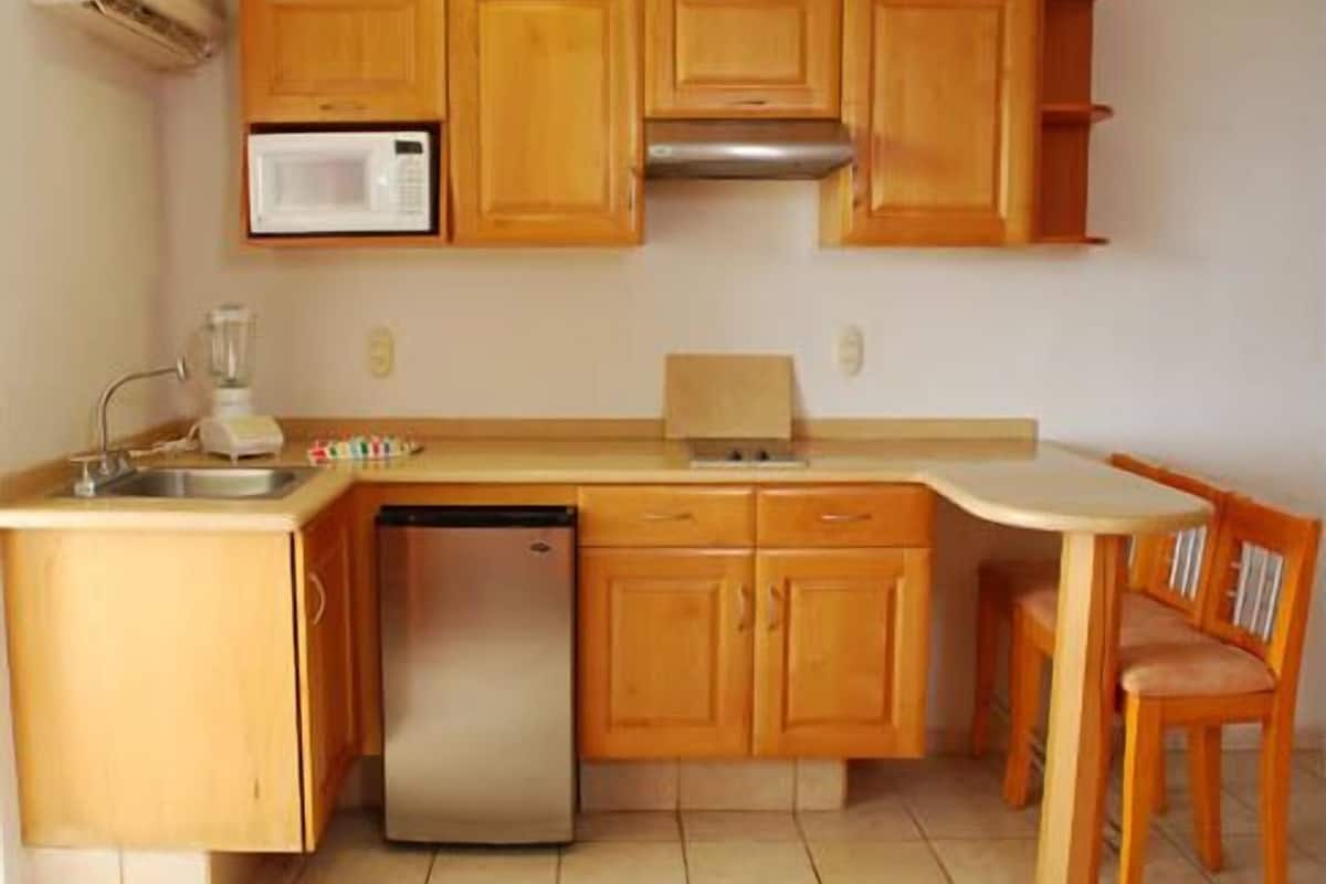 Une cuisine compacte avec des meubles en bois, un four à micro-ondes encastré, un lave-vaisselle et un petit coin repas avec une chaise.