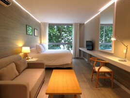 Habitación de hotel con cama, sofá, escritorio, televisor y ventana con vista a árboles.