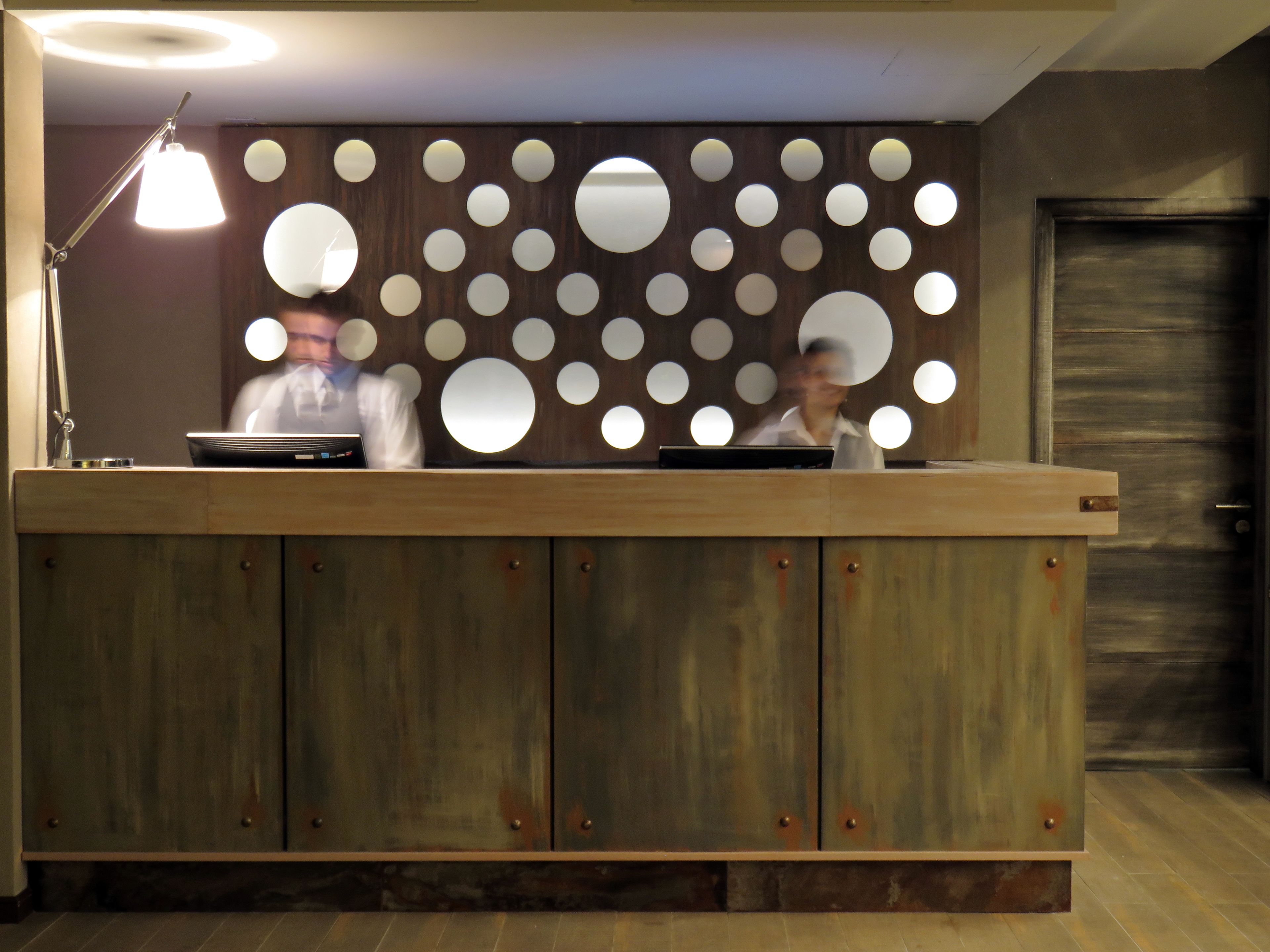 Un mostrador de recepción con detalles de madera y lámparas circulares en la pared.