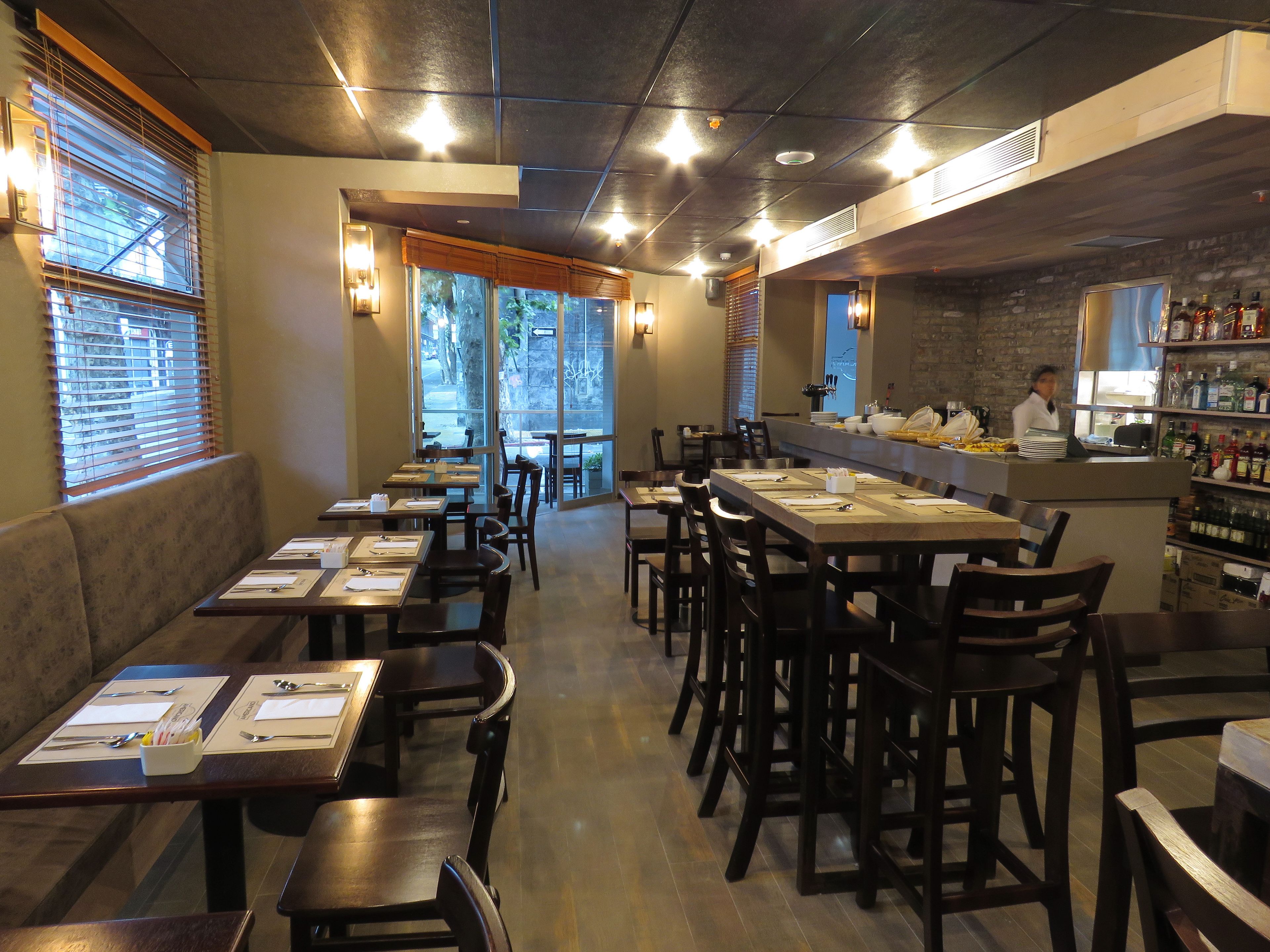 A restaurant with multiple dining tables and chairs, a bar area, and a view of the outdoors through large windows.