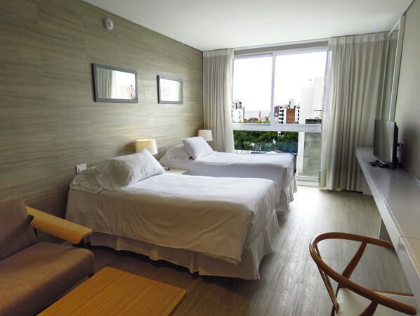 A hotel room with two beds, a sofa, a TV, and a balcony with a city view.