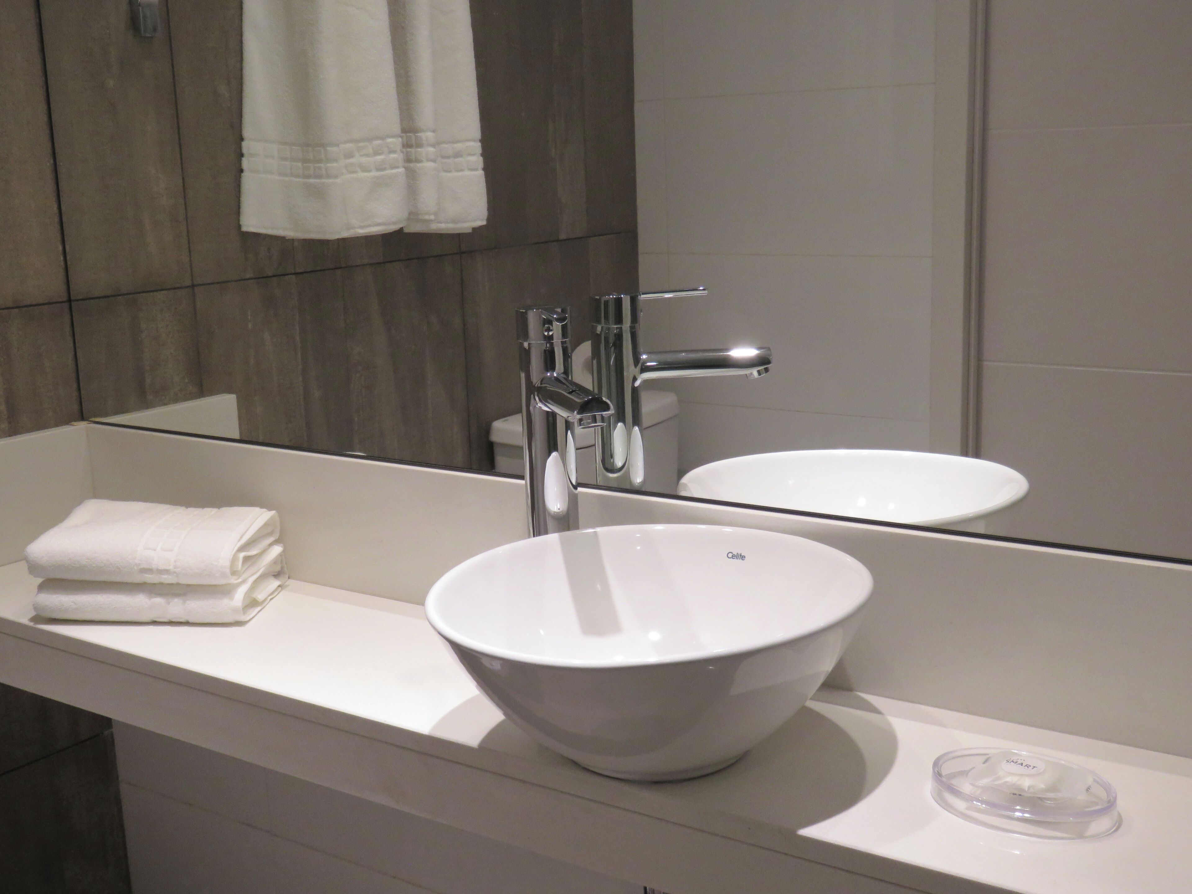 A modern bathroom with a white sink, a mirror, and a towel on the counter.