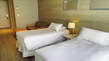 A hotel room with two beds, a desk with a lamp, a chair, and a wooden wall.