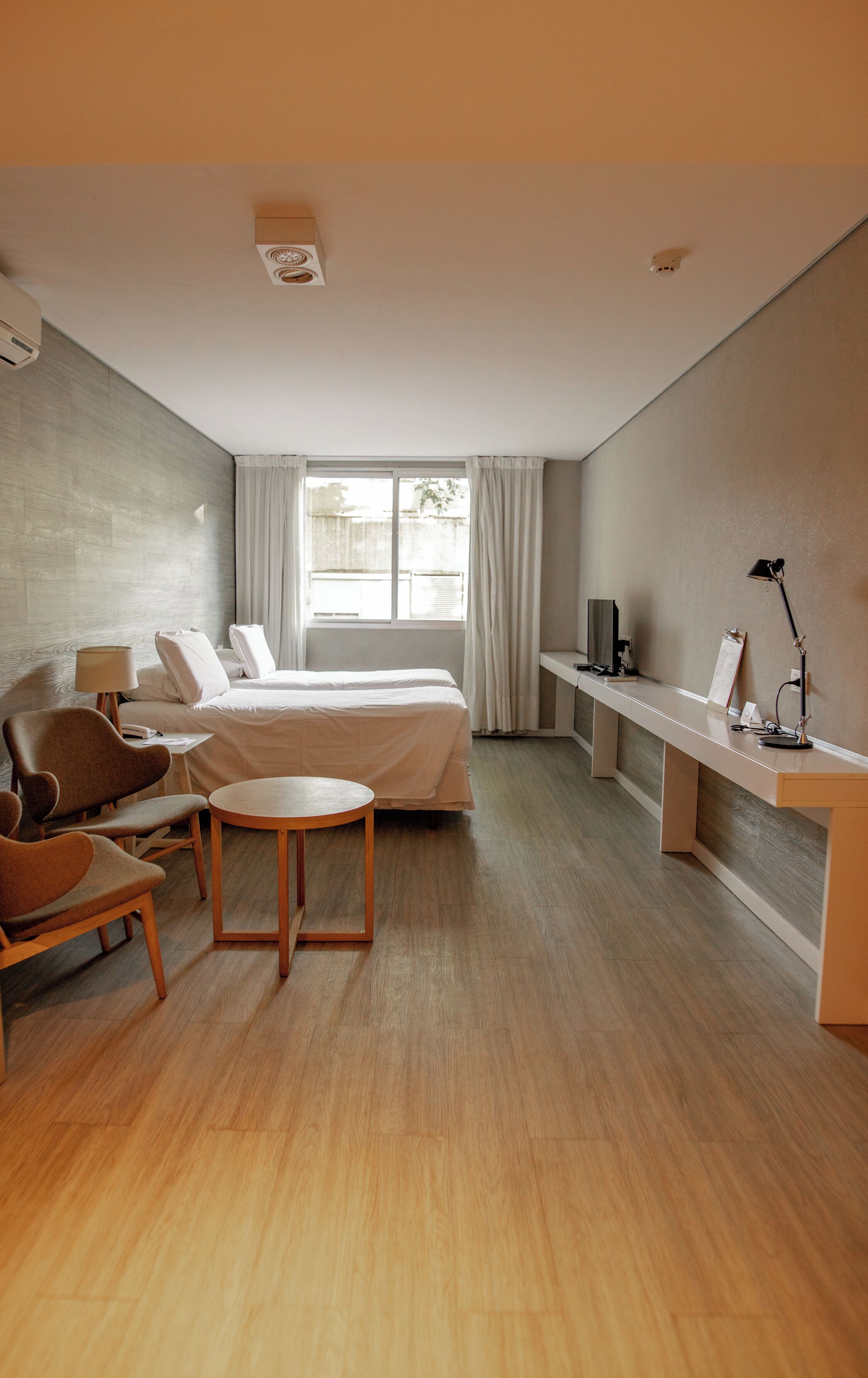 A modern hotel room with a bed, seating area, desk, and a large window.