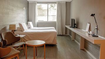 Une chambre d’hôtel moderne équipée d’un lit, d’un coin salon, d’un bureau et d’une grande fenêtre.