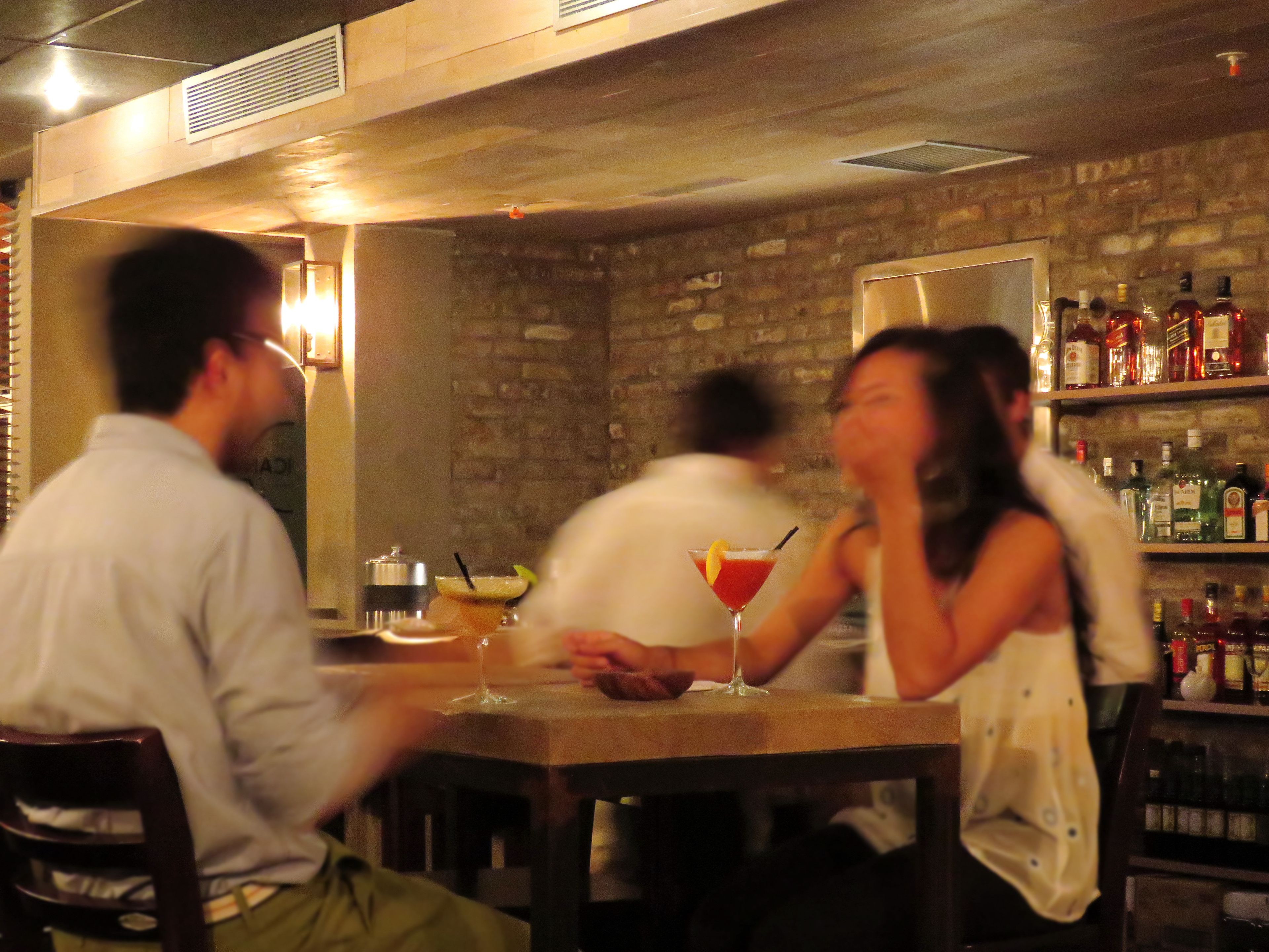 A bar area with a brick wall, wooden ceiling, and shelves with bottles.