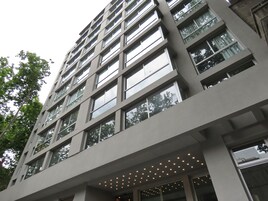 Un edificio moderno con varios pisos, grandes ventanales y un área de entrada cubierta con iluminación.