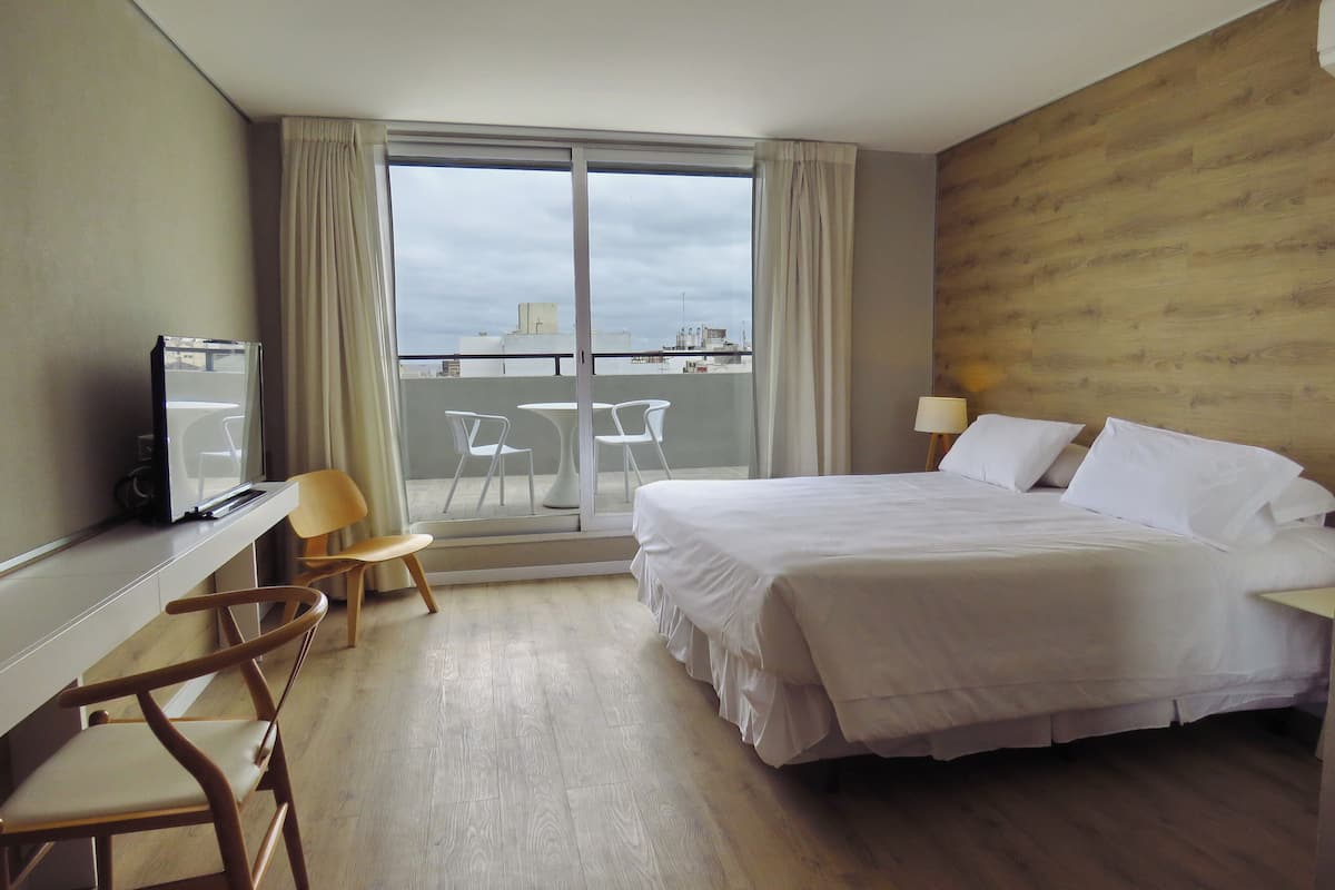 Quarto de hotel com cama, escrivaninha, cadeira, televisão e varanda com vista.