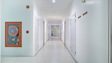 A long, narrow hallway with white walls and doors, a framed picture on the left, and a sign on the right.