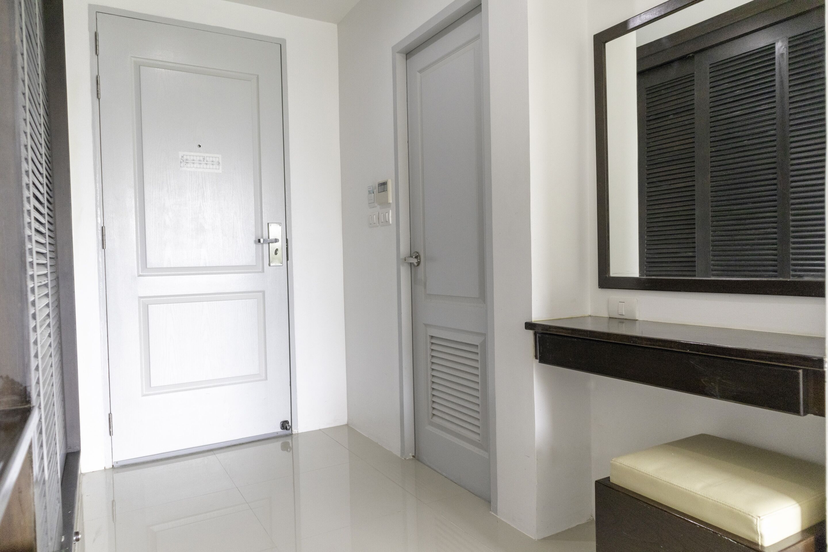 A hallway with a white door, a door with a louvered panel, and a dark counter with a light-colored bench.