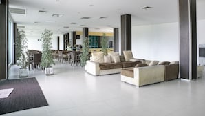 Un vestíbulo amplio con un sofá moderno, plantas en macetas y una mesa de recepción.