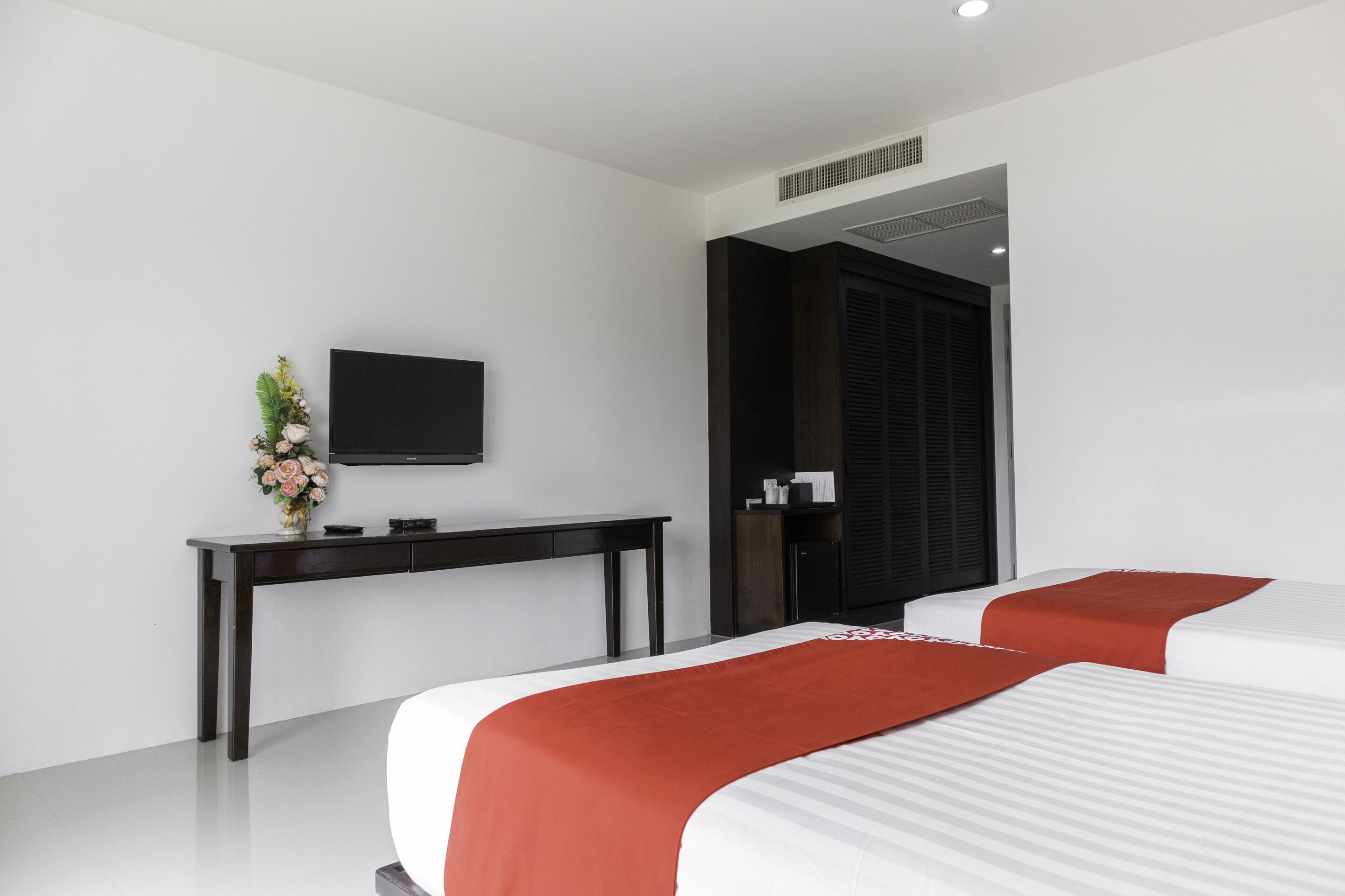 Ein modernes Hotelzimmer mit zwei Betten, einem Flachbildfernseher, einem Schreibtisch und einem dunklen Kleiderschrank.