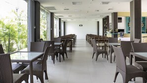 Un amplio espacio interior con filas de mesas y sillas, ventanas grandes y vistas al exterior con vegetación.