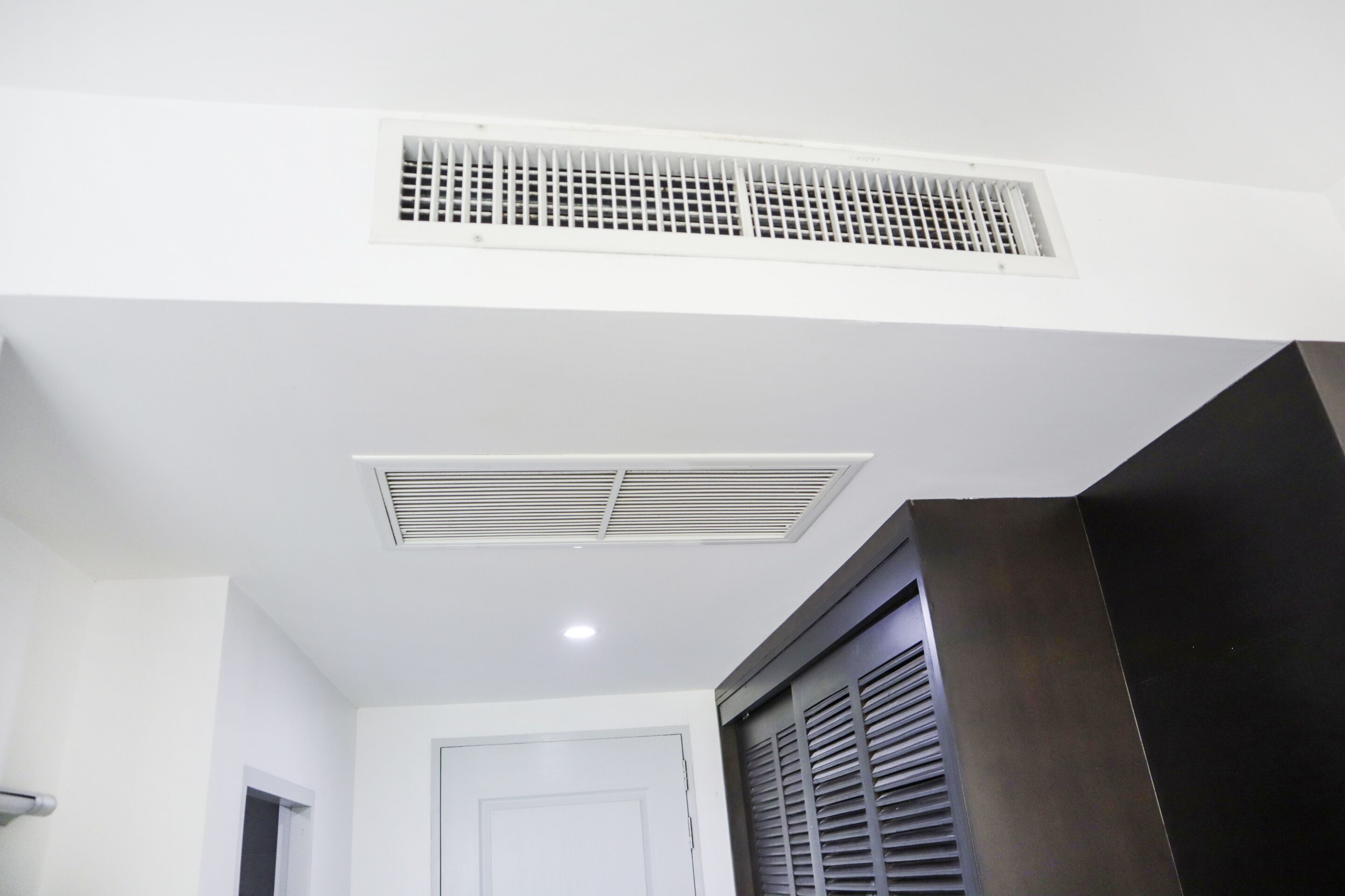 Una habitación con techo blanco, un respiradero, una puerta y una ventana con persianas.