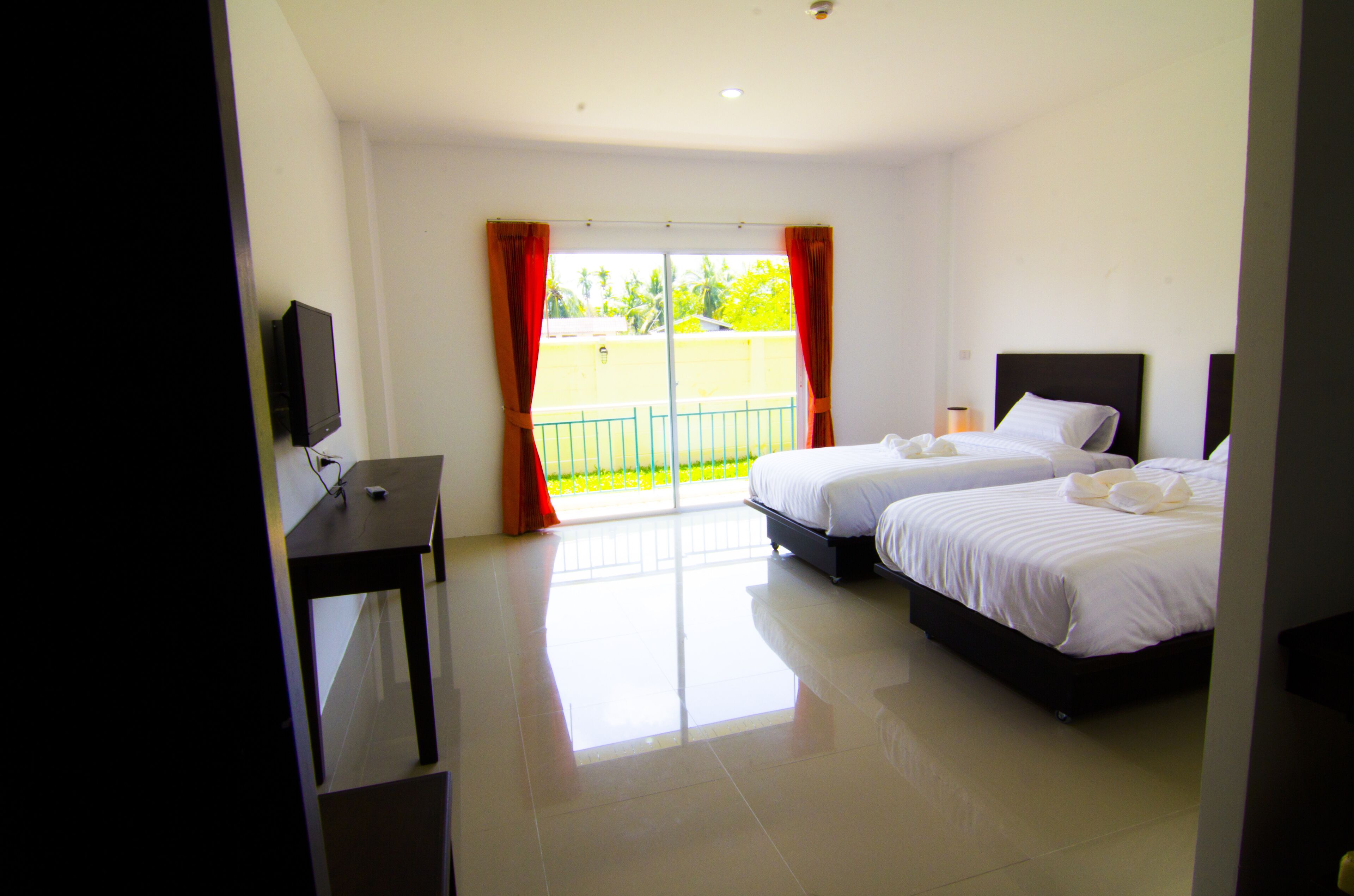 A hotel room with two beds, a TV, and a balcony with orange curtains.