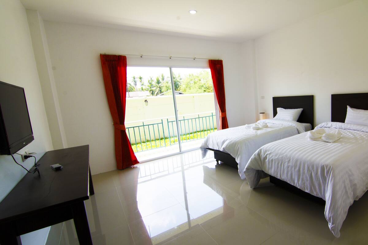Habitación de hotel con dos camas, un televisor y un balcón con cortinas rojas.