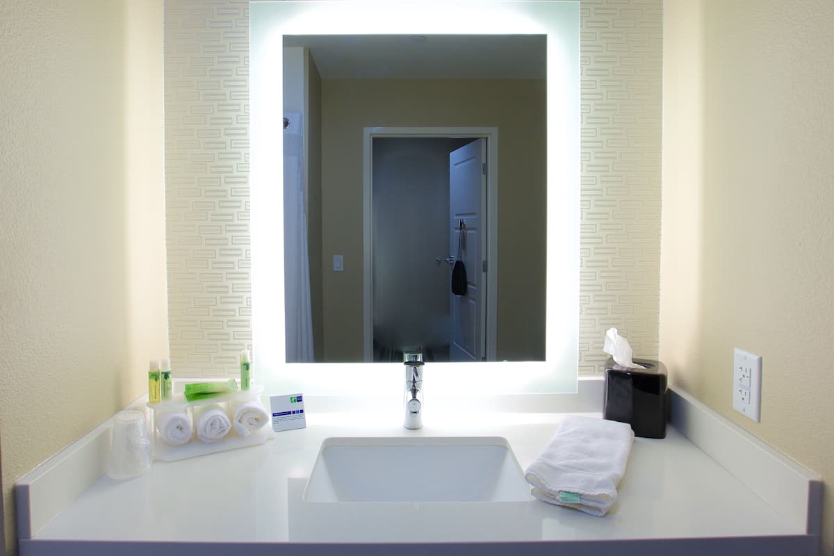A hotel bathroom with a large mirror, white sink, and toiletries.