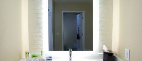 A hotel bathroom with a large mirror, white sink, and toiletries.