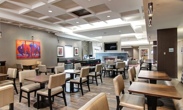 Un restaurant moderne doté de hauts plafonds, d’un éclairage encastré et d’une cheminée centrale. Les tables et les chaises sont disposées de manière à créer un espace propice aux repas.