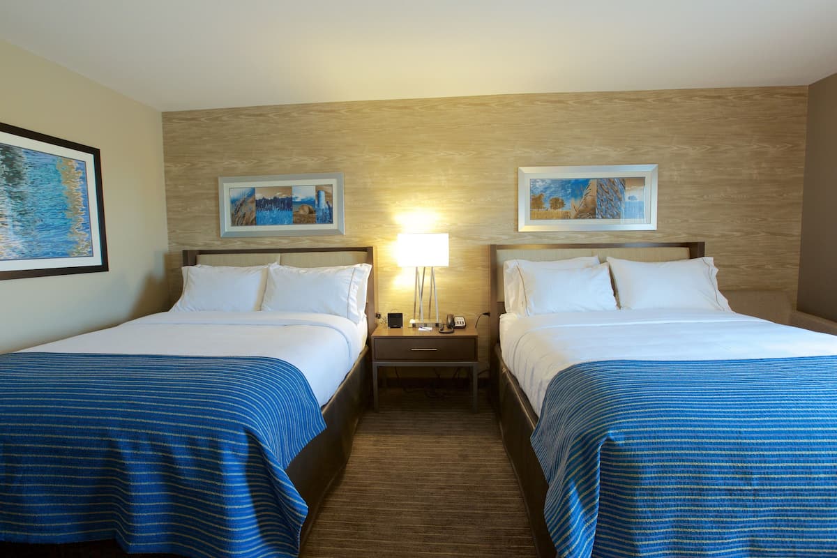 A hotel room with two beds, a nightstand, and a lamp. There are framed pictures on the wall.