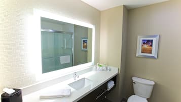 Un baño de hotel con un espejo grande, un lavamanos blanco, un inodoro y un cuadro en la pared.