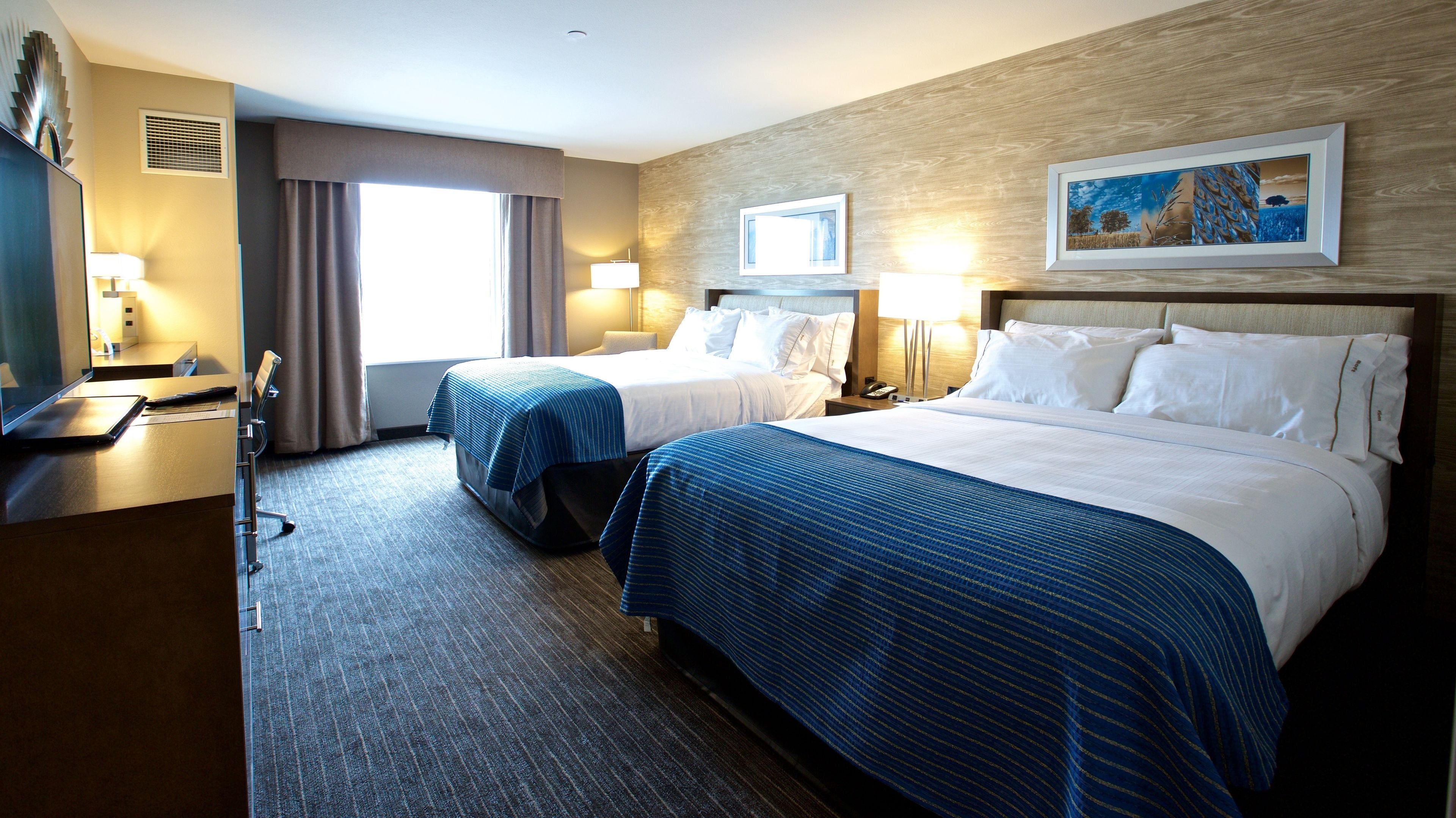 A hotel room with two beds, a desk, and a large window.