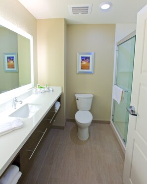 A bathroom with a white sink, mirror, and toilet. There is a framed picture on the wall and a towel rack. - Holiday Inn Express Fargo SW - I-94 Medical Center by IHG (Fargo)