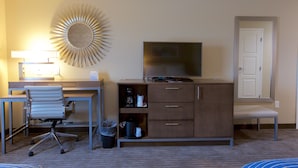 Ein Hotelzimmer mit Schreibtisch, Stuhl, Fernseher, Schrank und einer Wanddekoration im Sonnenstrahl-Design.