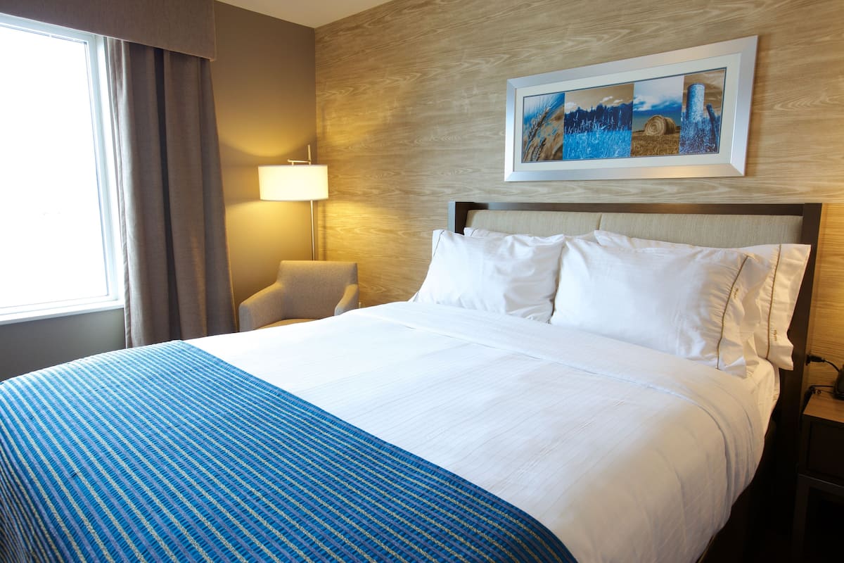 A hotel room with a large bed, a chair, a lamp, and a painting on the wall.