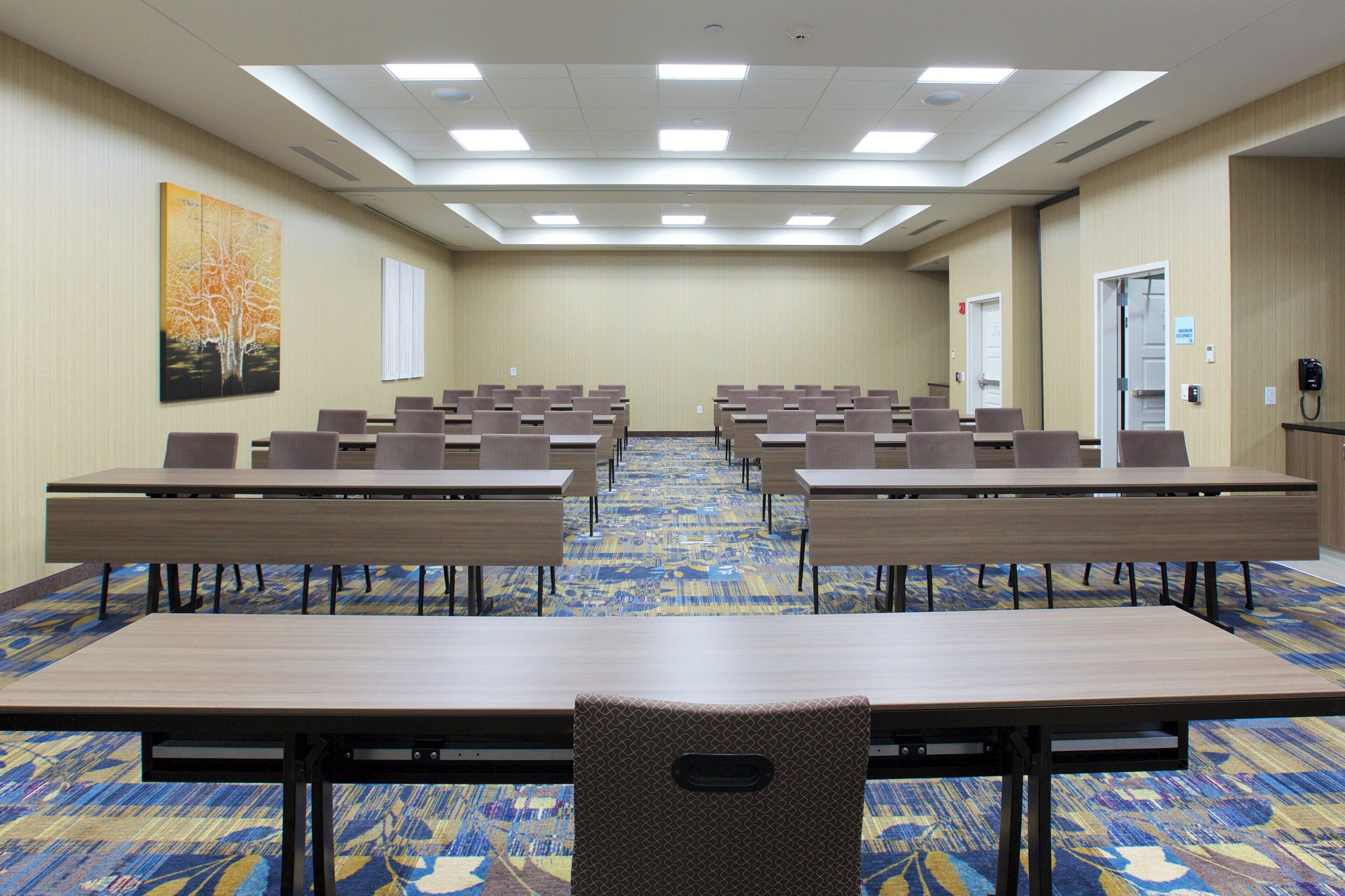 A conference room with multiple tables and chairs, a patterned carpet, and a painting on the wall.
