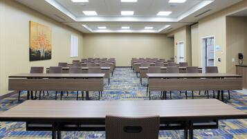 A conference room with multiple tables and chairs, a patterned carpet, and a painting on the wall.