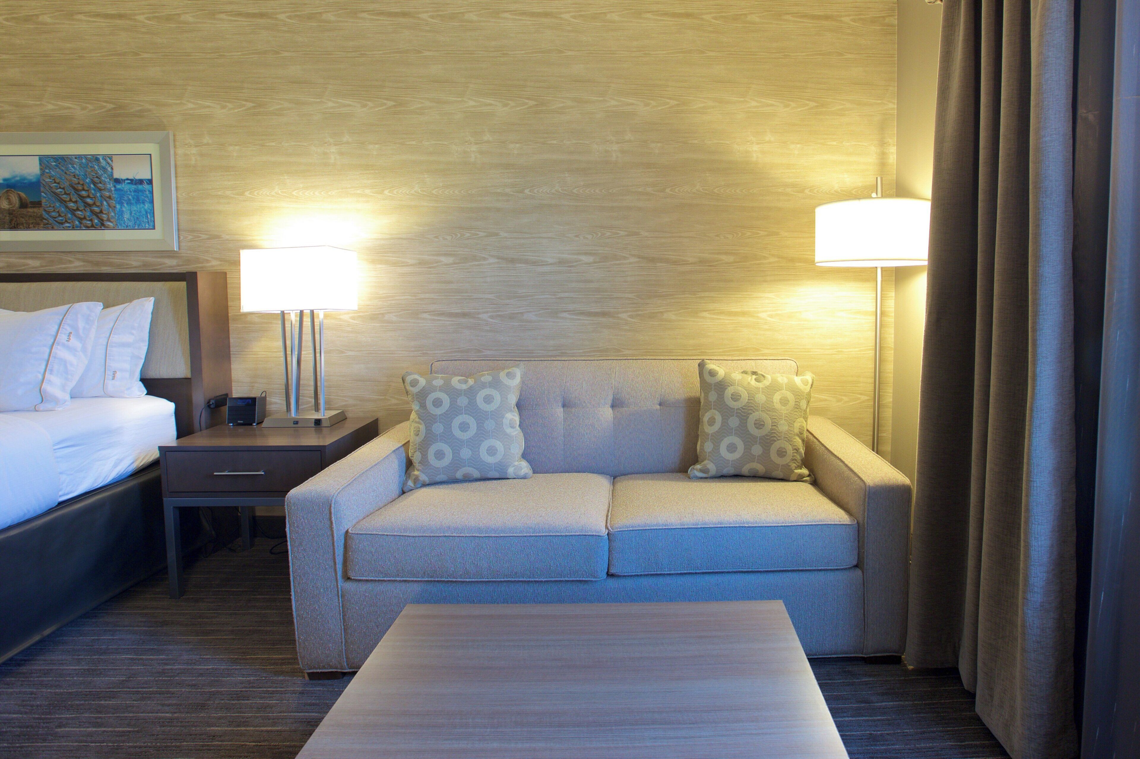 A hotel room with a bed, a sofa, a coffee table, and two lamps.