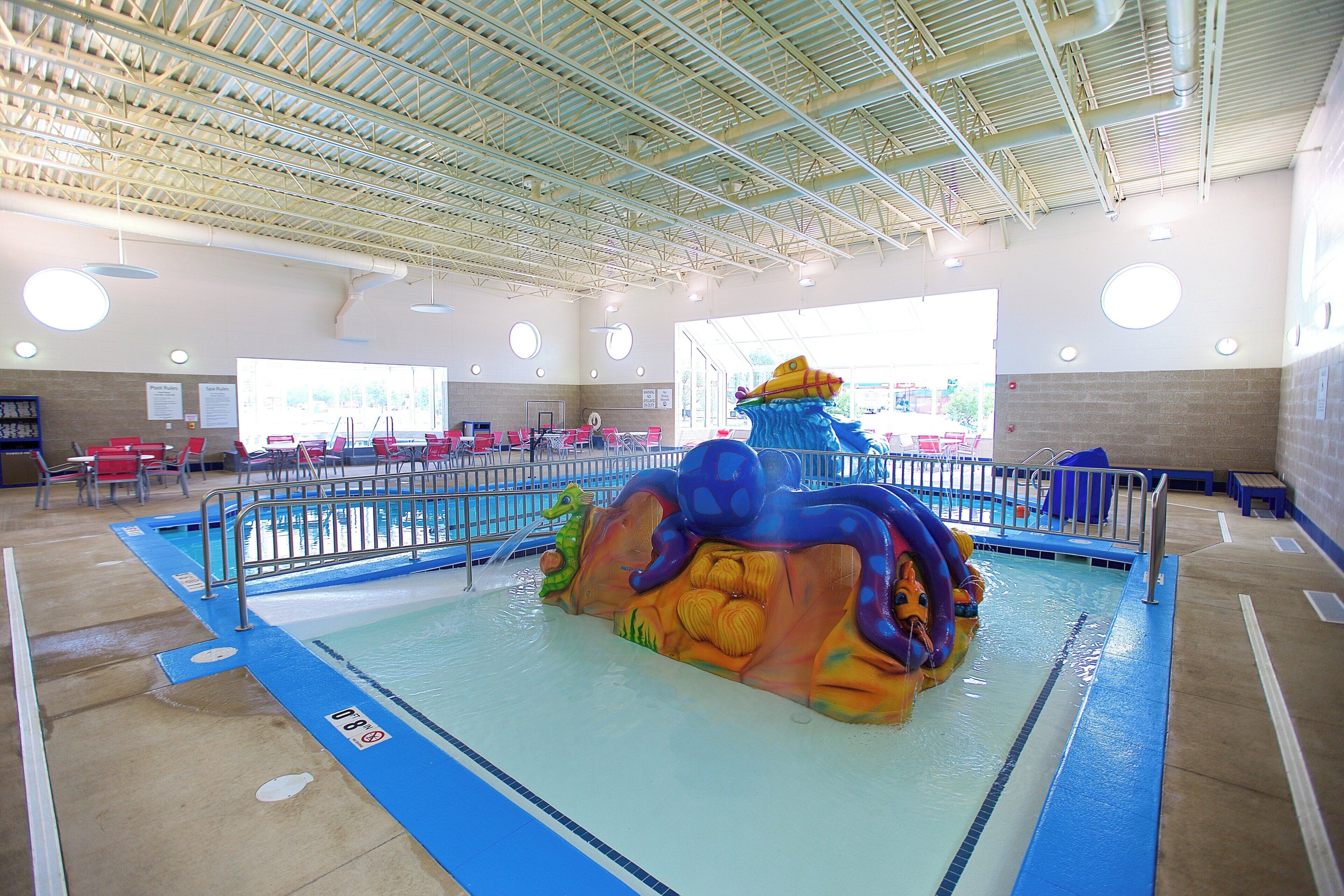 En indendørs swimmingpool med et farverigt vandrutsjeban og siddeområder.