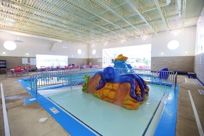 An indoor swimming pool with a colorful water slide and seating areas.