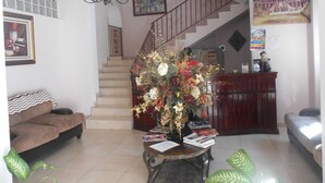 A living room with a staircase, a chandelier, a sofa, a coffee table with magazines, and a decorative vase. - Le Paradis S. Hotel (Cap-Haitien)