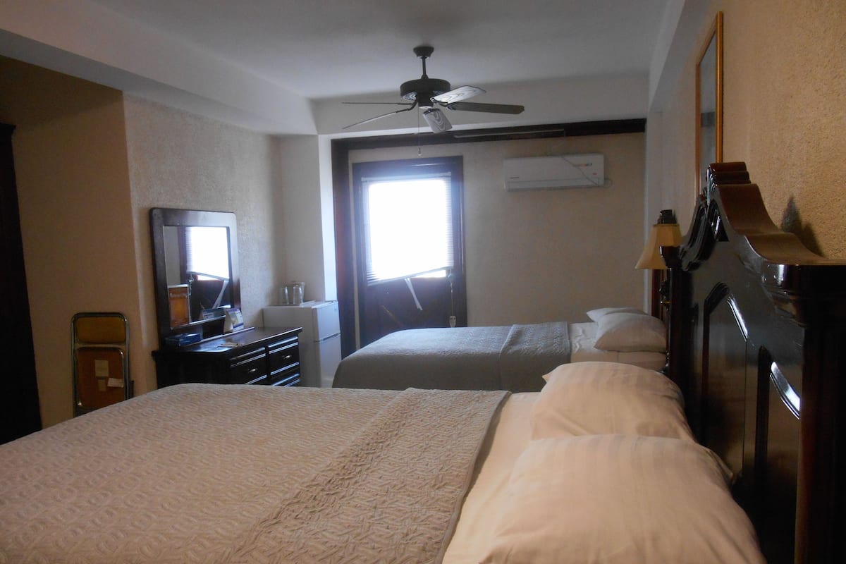 Ein Hotelzimmer mit zwei Betten, einem Deckenventilator, einem Schreibtisch mit Lampe und einem Spiegel.