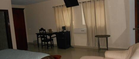 A hotel room with a bed, a desk with a chair, a small table, a sofa, and a TV mounted on the wall.