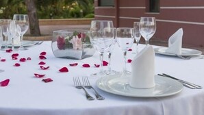 A table set for a meal with white tablecloth, clear glassware, and rose petals. - Hotel Mitra (Cabra)
