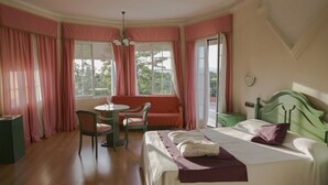 A bedroom with a bed, a chair, a table, and a window with curtains. - Hotel Mitra (Cabra)