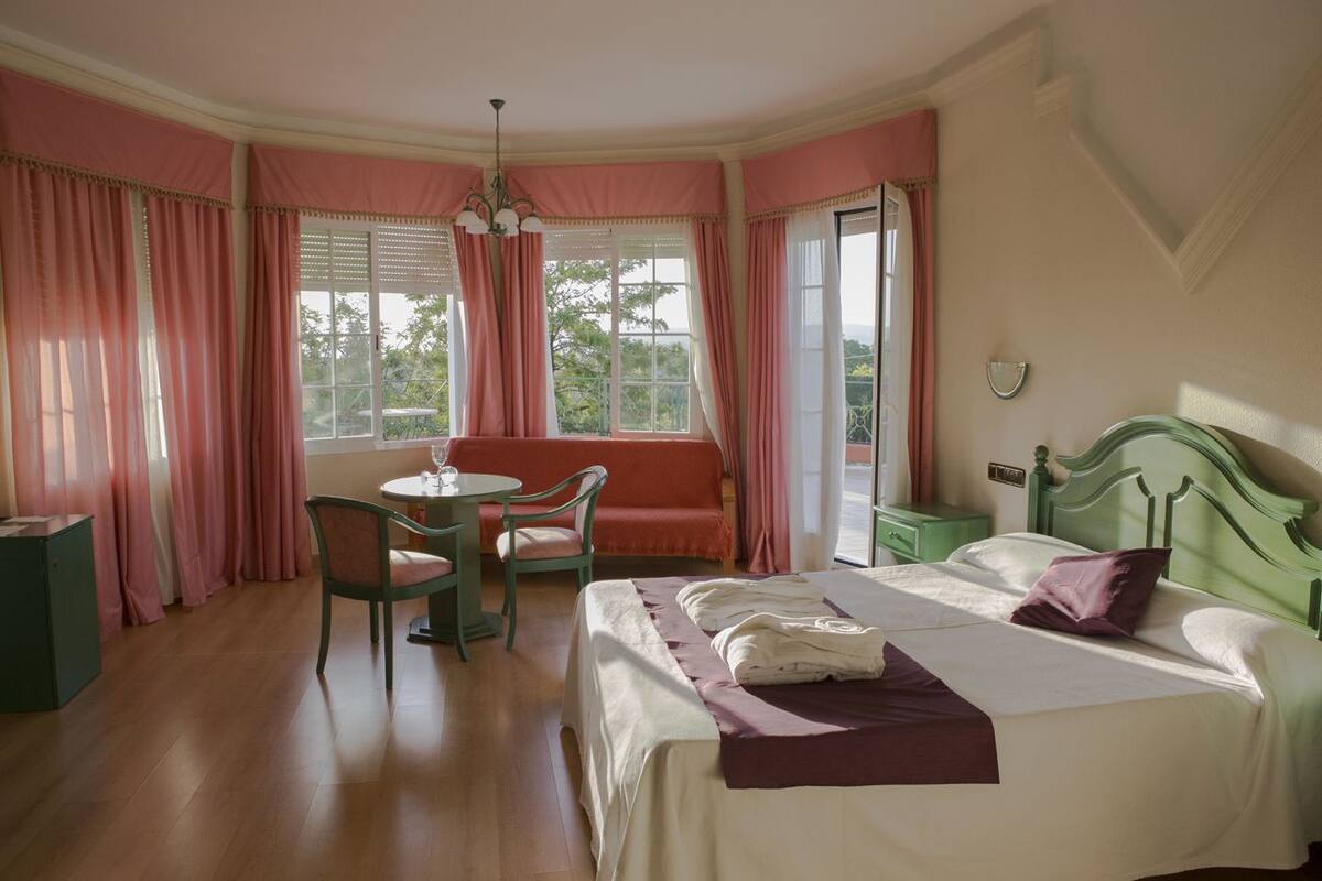 A bedroom with a bed, a chair, a table, and a window with curtains.