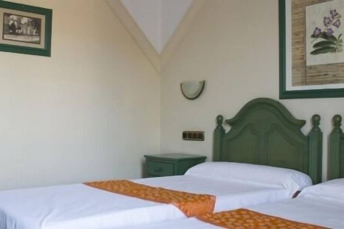 A room with two beds, a green headboard, a small nightstand, and a wall-mounted clock.