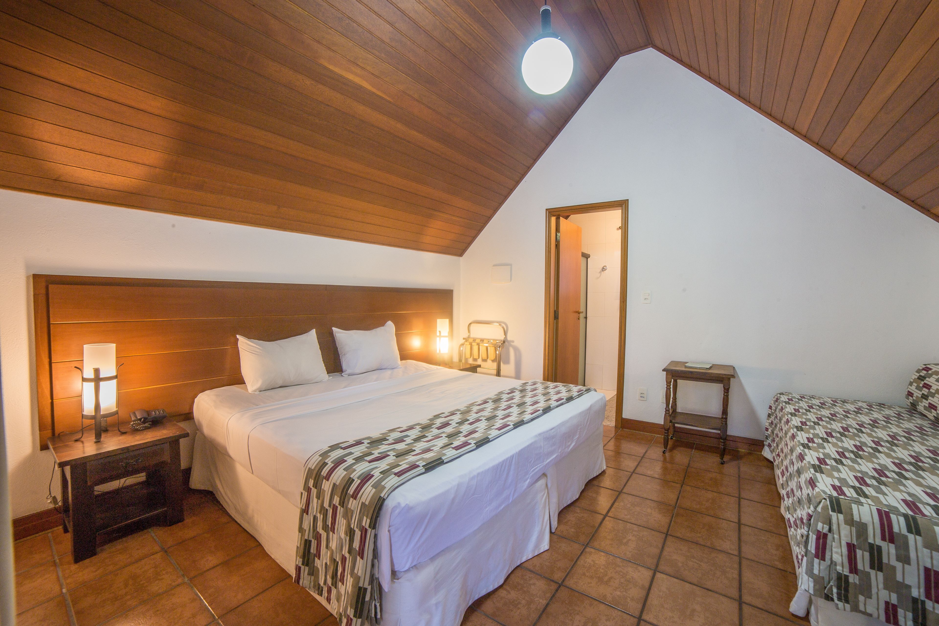 Ein Schlafzimmer mit Holzbalkendecke, einem Bett mit weißer Bettdecke, einem Nachttisch mit Lampe und einem kleinen Holzschemel.