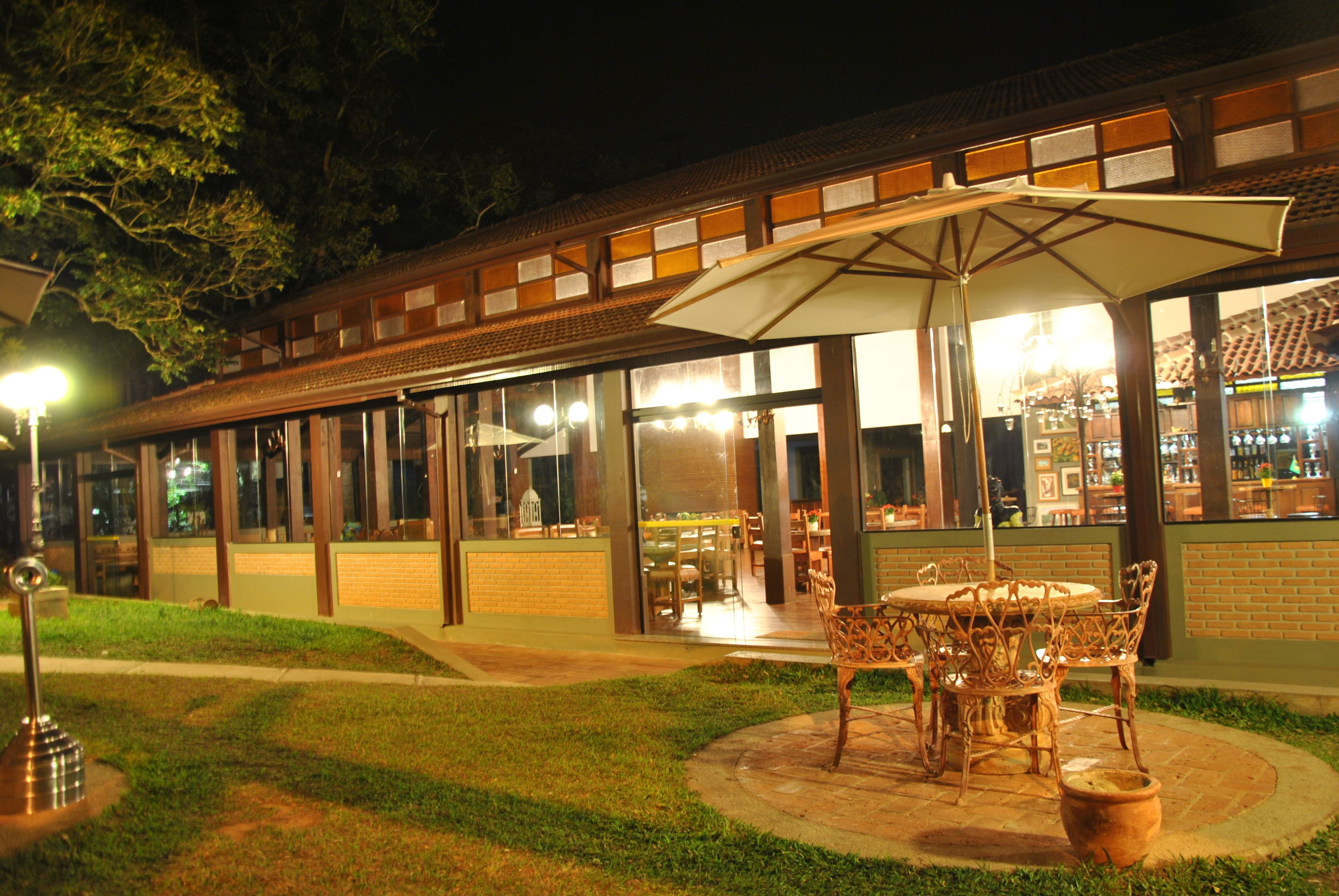 An outdoor patio area with a round table and chairs, surrounded by a glass enclosure, and a large umbrella providing shade.
