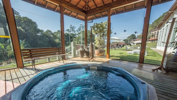 Een hottub in een overdekte buitenruimte met een houten terras, omringd door groen en uitzicht op een woonwijk.