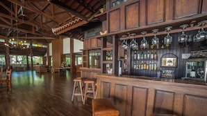 Een bar met houten meubels, krukken en diverse flessen en glazen op planken.