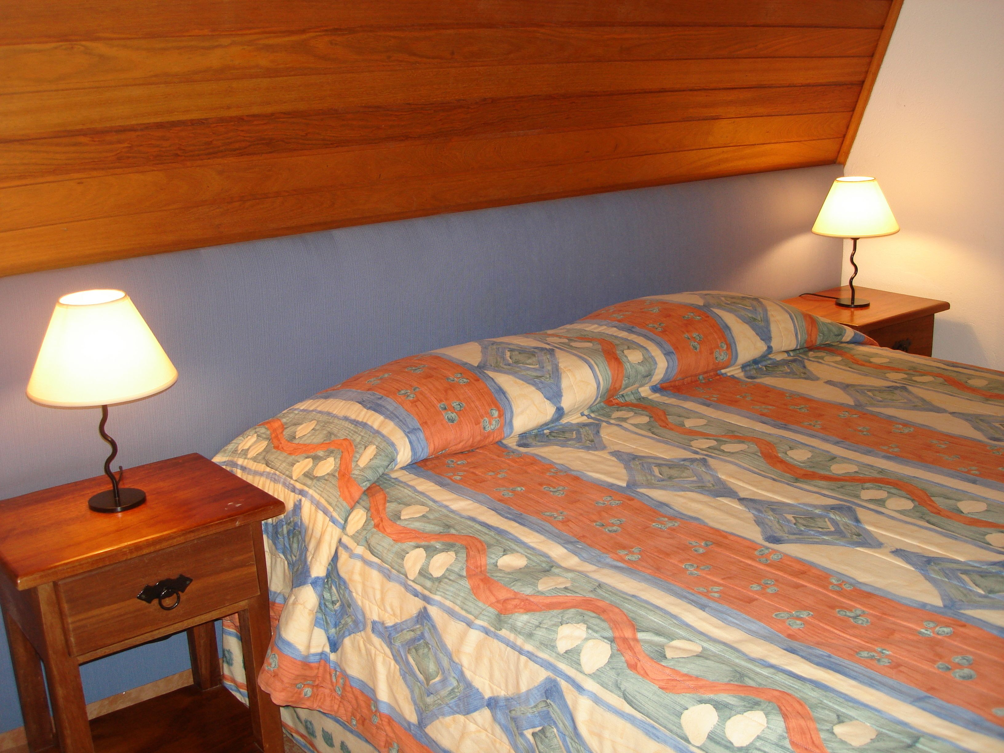A bedroom with a wooden headboard, two bedside tables with lamps, and a patterned bedspread.