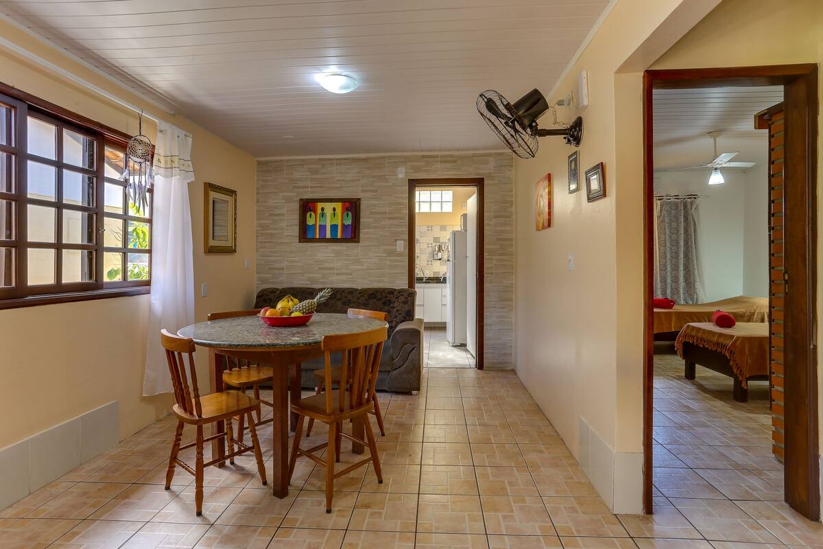 A dining area with a round table and chairs, a sofa, and a kitchen visible in the background.