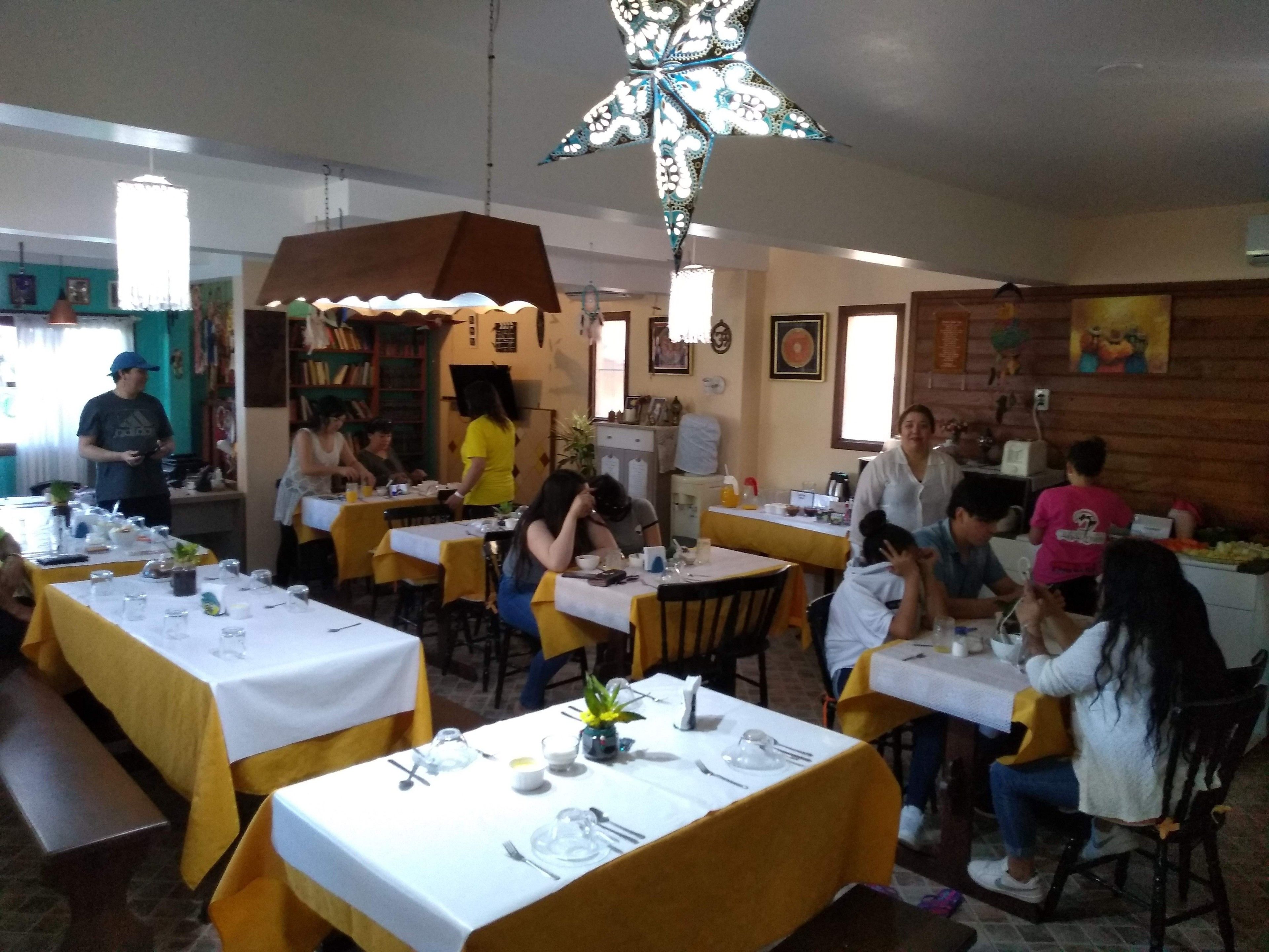 Un restaurante con mesas dispuestas para comer, una lámpara decorativa grande en el techo y una pared de madera con obras de arte.